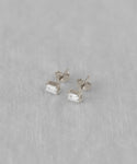 The Ivy Emerald Cut Studs feature clear gemstones set in white gold with butterfly backs, elegantly displayed on a soft, light gray fabric background.