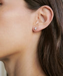 Close-up of a womans ear adorned with Ivy Emerald Cut Studs in white gold. The neutral background emphasizes the earrings elegant rectangular shape, while her brown hair is tucked neatly behind her ear.