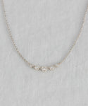The Violette Diamond Necklace in white gold features a pendant with five small round diamonds in a row, displayed on a light gray textured fabric background.