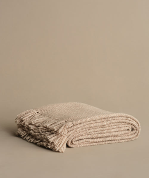 The Alpaca Basketweave Throw, handwoven in Peru from superfine alpaca and featuring fringed edges, is shown folded on a plain beige background.