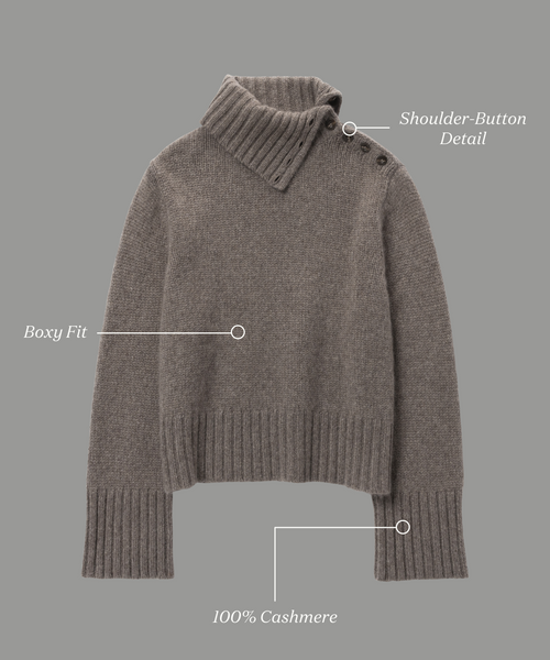 The Cashmere Jackie Sweater is a gray, boxy-fit piece crafted from 100% cashmere, featuring a luxe knit texture, ribbed cuffs and hem, and stylish shoulder-button detail. Labels highlight Boxy Fit and Shoulder-Button Detail.