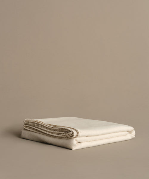 The Chateau Alpaca Coverlet, neatly folded, rests on a smooth beige surface against a plain beige background, adding a touch of elegance.