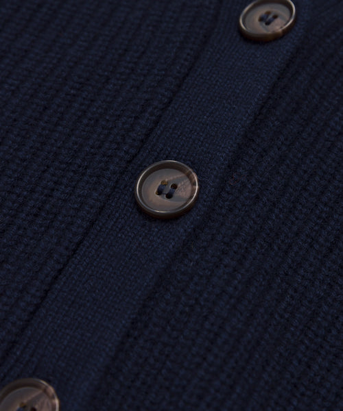 Close-up of navy blue knit fabric from the Cropped Cashmere Cocoon Cardigan, showing a vertical line of brown plastic buttons sewn onto a smooth, solid strip.