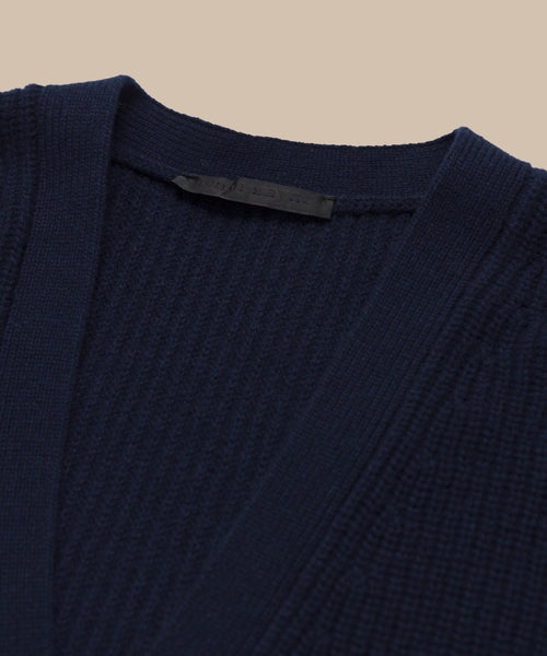 Close-up of the Cropped Cashmere Cocoon Cardigan in navy, featuring a ribbed knit texture, V-neckline, and a black fabric tag inside the collar, displayed against a neutral beige background.