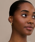 A woman with smooth brown skin and glossy lips wears Felix Dome Hoops. Her hair is pulled back, makeup is subtle with soft eyeshadow and blush, and she completes the look with these elegant fine jewelry hoops.