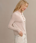 A woman with long blonde hair stands in profile against a neutral background, wearing the Grayson Pullover in light beige and cream-colored pants.