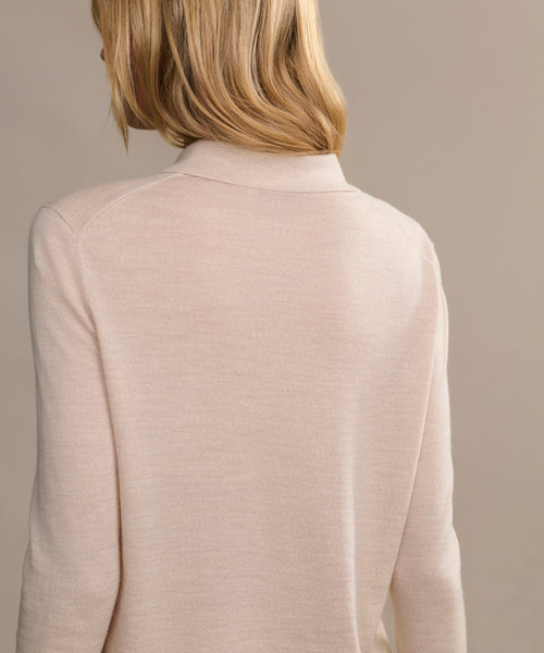 A person with shoulder-length blonde hair is seen from behind wearing the Grayson Pullover, a light beige casual polo with a small collar, set against a neutral background.