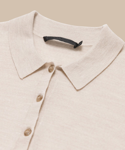 A close-up of the Grayson Pullover, a beige casual polo with a button-down front featuring three visible buttons and an inner black label, laid flat on a matching beige background.