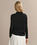 A person with blonde hair is shown from the back, wearing the Grayson Pullover in black and a white skirt, standing against a plain beige background.
