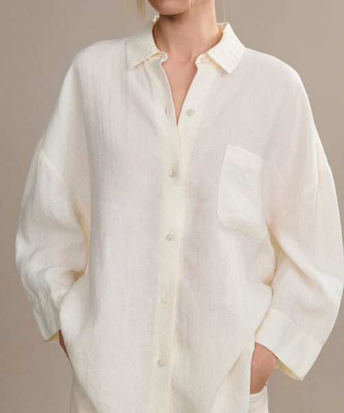 Wearing the Linen Logan Shirt—a loose-fitting, off-white, boxy-fit button-up with a front pocket—this person exudes effortless style, their hands in pockets and the upper part of their face just out of frame.