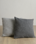 Two Alpaca Basketweave Pillows sit on a table, their soft texture enhancing the space with cozy elegance.