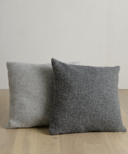 Two Alpaca Basketweave Pillows sit on a table, their soft texture enhancing the space with cozy elegance.