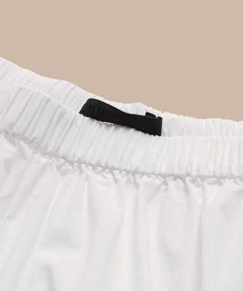 Close-up of the waistband of the Lauren Skirt, a true wardrobe staple in white elastic, featuring a small black fabric tag at the back against a beige background.