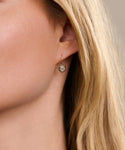 Close-up of a womans ear adorned with Liv Rose Cut Earrings—delicate gold earrings featuring a round gemstone in a two-tone setting. Her smooth skin and blonde hair partially frame the elegant jewelry.