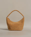 The Medium Crescent Bag, crafted in Italy from luxe tan suede with a thick twisted handle, is displayed on a plain light beige background.