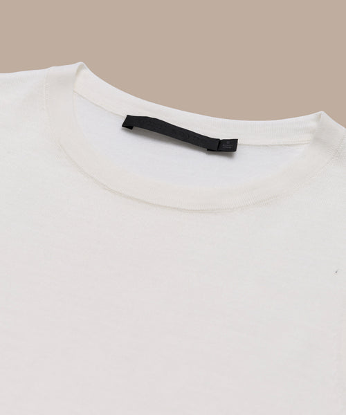 A close-up of a plain white Merino Tank laid flat on a beige surface, highlighting the collar and black label inside the neckline—an ideal base layer for any outfit.