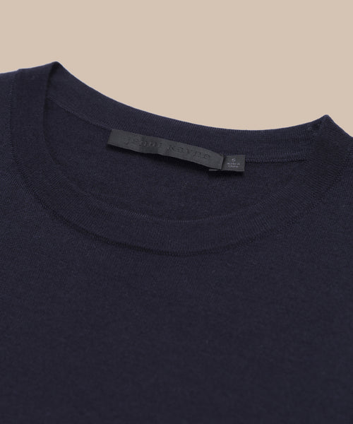 A close-up of the neckline and upper chest area of the Merino Tank in dark navy blue, perfect as a stylish base layer, with a visible black label inside the collar, set against a beige background.