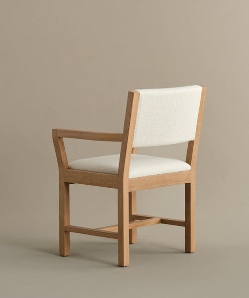 The Montecito Upholstered Dining Arm Chair features a white oak frame in light brown with a white upholstered seat and backrest, armrests, and a simple modern design, shown against a plain beige background.