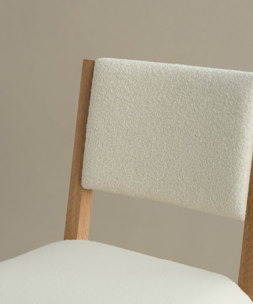 A close-up of the Montecito Upholstered Dining Chair, featuring a white oak frame and ivory boucle seat and backrest, set against a plain beige background.