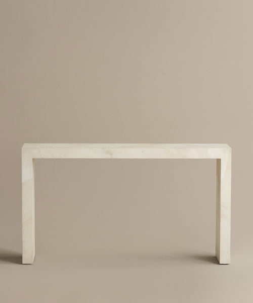 The Napa Console Table is a minimalist ivory piece featuring clean, straight lines and light-colored marble, set against a plain beige background for a simple, elegant look with no visible embellishments.