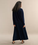 A person with long curly hair, seen from behind, models the Pleated Skirt in dark navy with a matching sweater and black open-toe heels against a plain beige background.