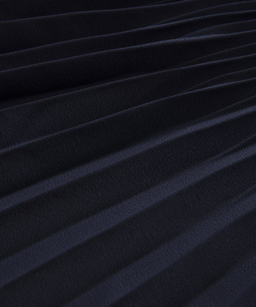 Close-up of the Pleated Skirt’s dark fabric, featuring evenly spaced diagonal pleats that create a textured pattern. The material looks soft with a subtle sheen.