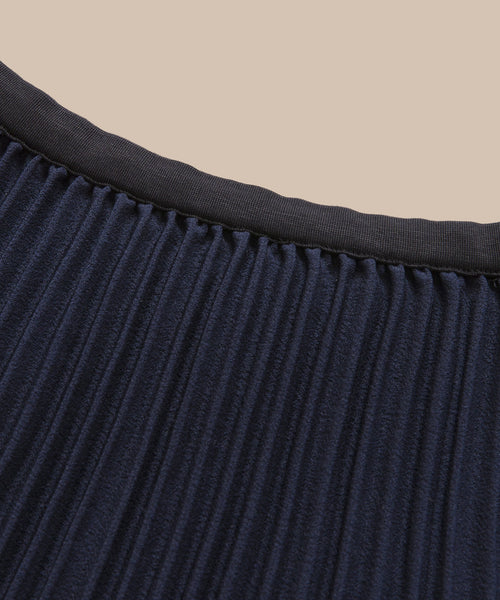 Close-up of the Pleated Skirt in navy with a black waistband, displayed against a beige background.