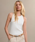 A woman with long blonde hair wears the Cotton Rib Tank, light beige pants, and a beige belt. She stands with one hand in her pocket against a neutral background, looking confidently at the camera.