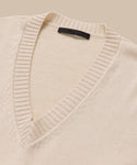 Simone V-Neck sweater in ivory, crafted from fine cotton-merino blend with a ribbed collar and black neck label, offers a touch of luxury—shown here on a beige background.