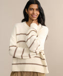 A woman with long dark hair smiles while wearing the Chloe Crewneck, a cropped sweater with light brown stripes, and tan pants, standing against a neutral beige background.