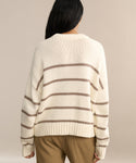 A person with long dark hair, seen from behind, is wearing the Chloe Crewneck—a cream-colored sweater with beige stripes and a cropped fit—paired with tan pants against a plain neutral background.