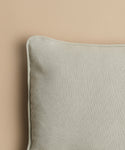 A close-up of the Adler Lumbar Pillow, featuring linen-blend fabric and a piped edge, is shown against a plain beige background with only the upper left part of the pillow visible.