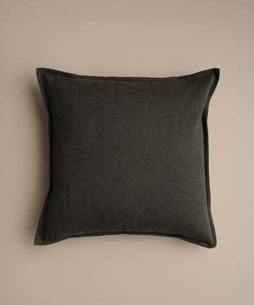 The Adler Pillow, featuring a square shape and dark gray color with a smooth texture, is set against a plain beige background, bringing understated luxury to any decor.