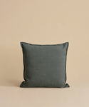 A dark gray Adler Pillow is centered against a beige background, showcasing its smooth Belgian linen cover. The luxury pillow appears plump and soft, highlighting its simple yet elegant design.