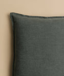A close-up of the dark grey Adler Pillow in Belgian linen, highlighting its texture and top left corner against a plain beige background.