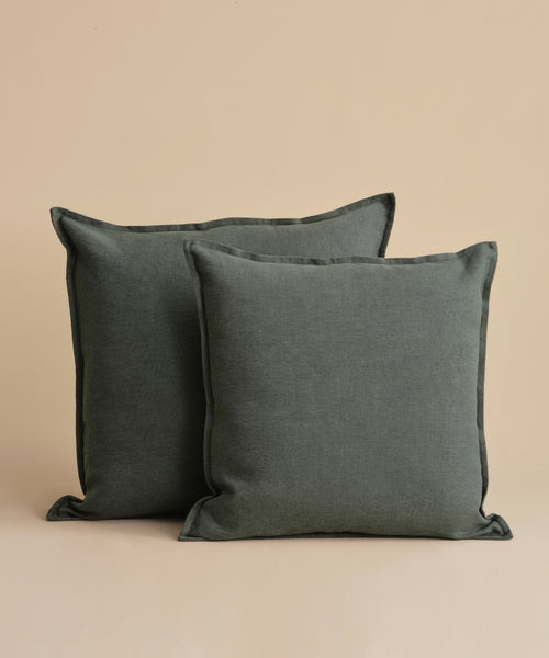 Two Adler Pillows in plain dark green, crafted from soft Belgian linen, are placed side by side against a beige background. These throw pillows feature a simple design and inviting texture.