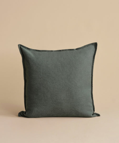The Adler Pillow, featuring a square shape and soft Belgian linen texture in dark gray, is displayed upright against a plain beige background.