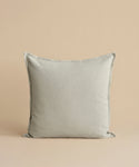 The Adler Pillow, featuring a square shape and light gray hue in a premium linen blend, stands upright against a simple beige background.