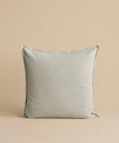 The Adler Pillow, featuring a square shape and light gray hue in a premium linen blend, stands upright against a simple beige background.