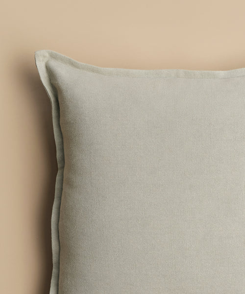 A close-up of the Adler Pillow, made from a linen blend with a visible seam edge, is shown against a beige background, displaying only its upper left portion.