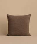 The Alpaca Basketweave Pillow, a handmade square brown cushion from Peru, is displayed upright against a beige background.