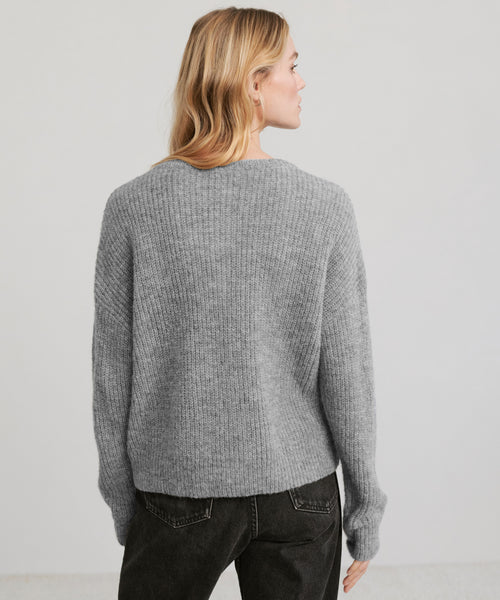 A person with long blonde hair is shown from the back, wearing the Hayes Crewneck Cardigan in gray and black jeans against a plain light background.