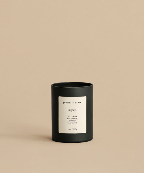 The Aspen Glass Candle, 10oz/285g, features a black glass vessel with a white label and notes of Balsam Fir, Eucalyptus, and Grapefruit. Made from a natural wax blend and hand-poured in Los Angeles, it sits against a plain beige background.