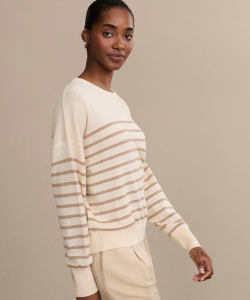 A woman with short hair wears the Avery Crewneck sweater and matching pants, standing against a plain beige background and looking at the camera with a slight smile.