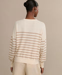 A person with their hair in a bun is shown from the back, wearing the Avery Crewneck striped sweater in lightweight knit and matching cream pants against a plain beige background.