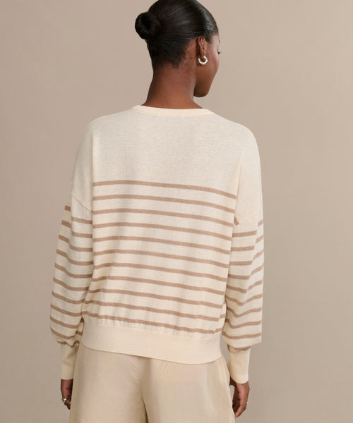 A person with their hair in a bun is shown from the back, wearing the Avery Crewneck striped sweater in lightweight knit and matching cream pants against a plain beige background.