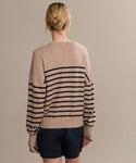 A person with blonde hair in a low bun is seen from behind, wearing the Avery Crewneck striped sweater and dark shorts, standing before a plain beige background for an effortless coastal vibe.