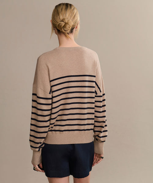 A person with blonde hair in a low bun is seen from behind, wearing the Avery Crewneck striped sweater and dark shorts, standing before a plain beige background for an effortless coastal vibe.
