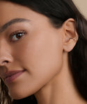 A close-up of a woman with dark hair and smooth skin, wearing the Loren Pearl Ear Cuff from Jenni Kayne Jewelry. The focus is on her eye, ear adorned with the modern cuff, and her neutral expression.