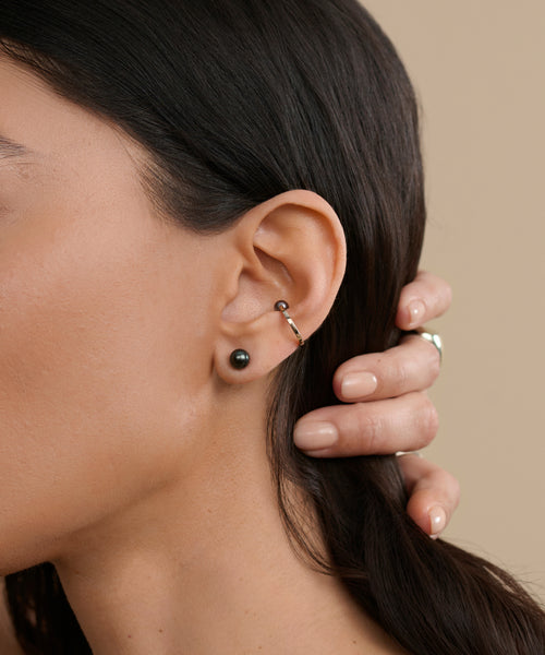 Close-up of a woman's ear wearing Modern Elegance Jewelry's Medium Loren Pearl Studs in the lobe and a silver hoop in the cartilage. Her manicured hand touches her hair, highlighting her refined style.